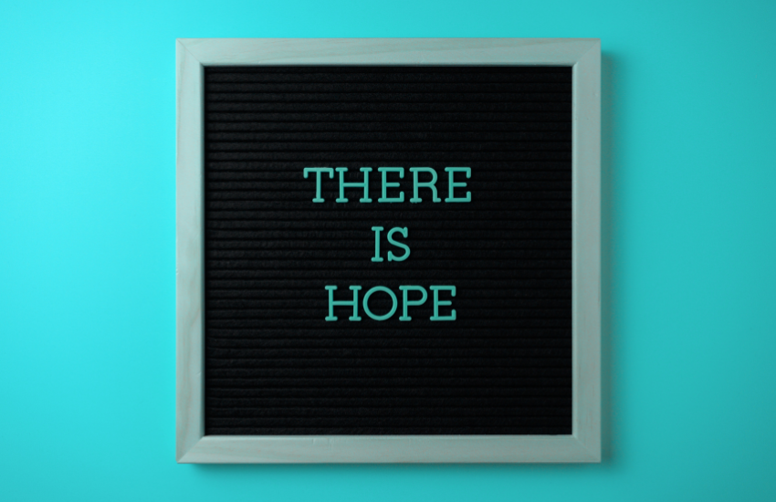 Close-up of a framed, black fall letter board hanging on a blue wall with the inspirational quote 'THERE IS HOPE' written in teal-colored letters.